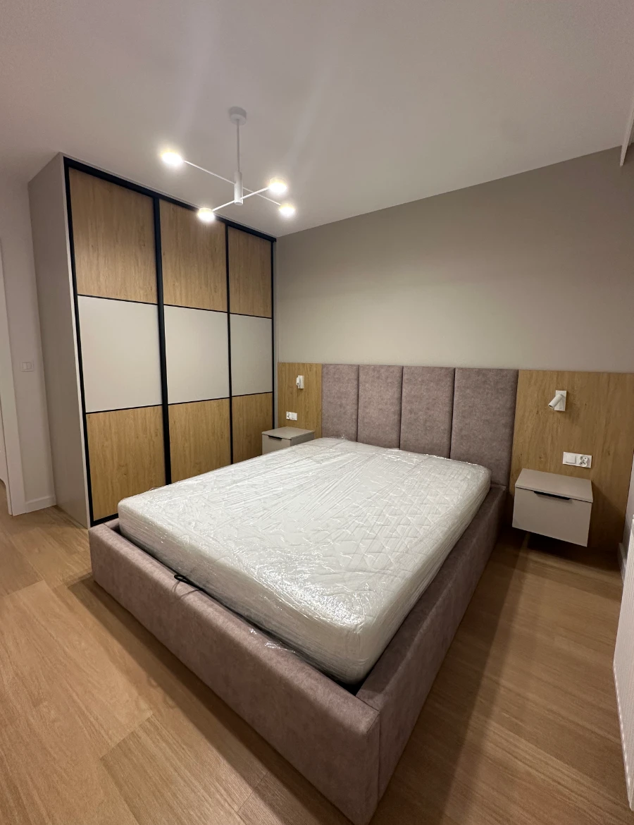 Sypialnia z dużym łóżkiem z oparciem, lampkami nocnymi i szafą przesuwną po prawej stronie