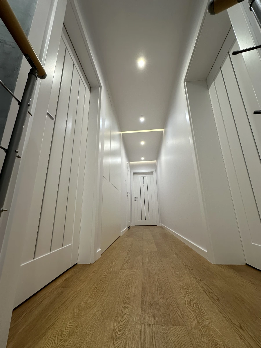 Jasny, biały korytarz z drewnianą podłogą i naturalnym oświetleniem