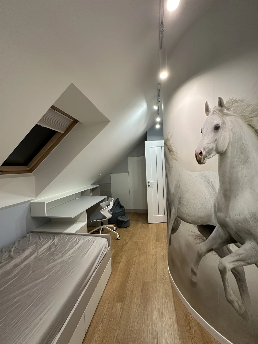 Widok z łóżka na biurko w pokoju na poddaszu z grafiką galopujących koni