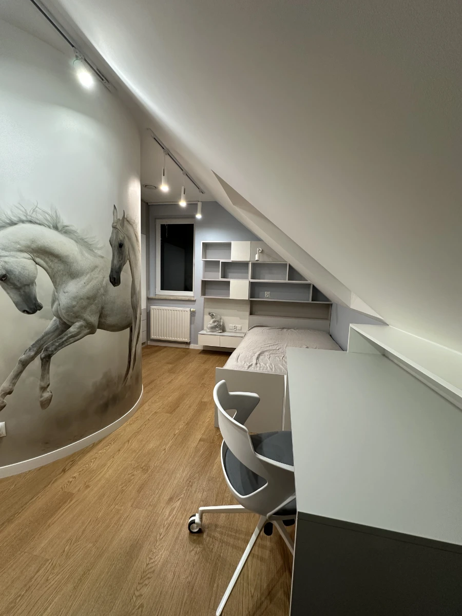 Pokój na poddaszu z biurkiem, łóżkiem i grafiką białych koni w galopie na ścianie