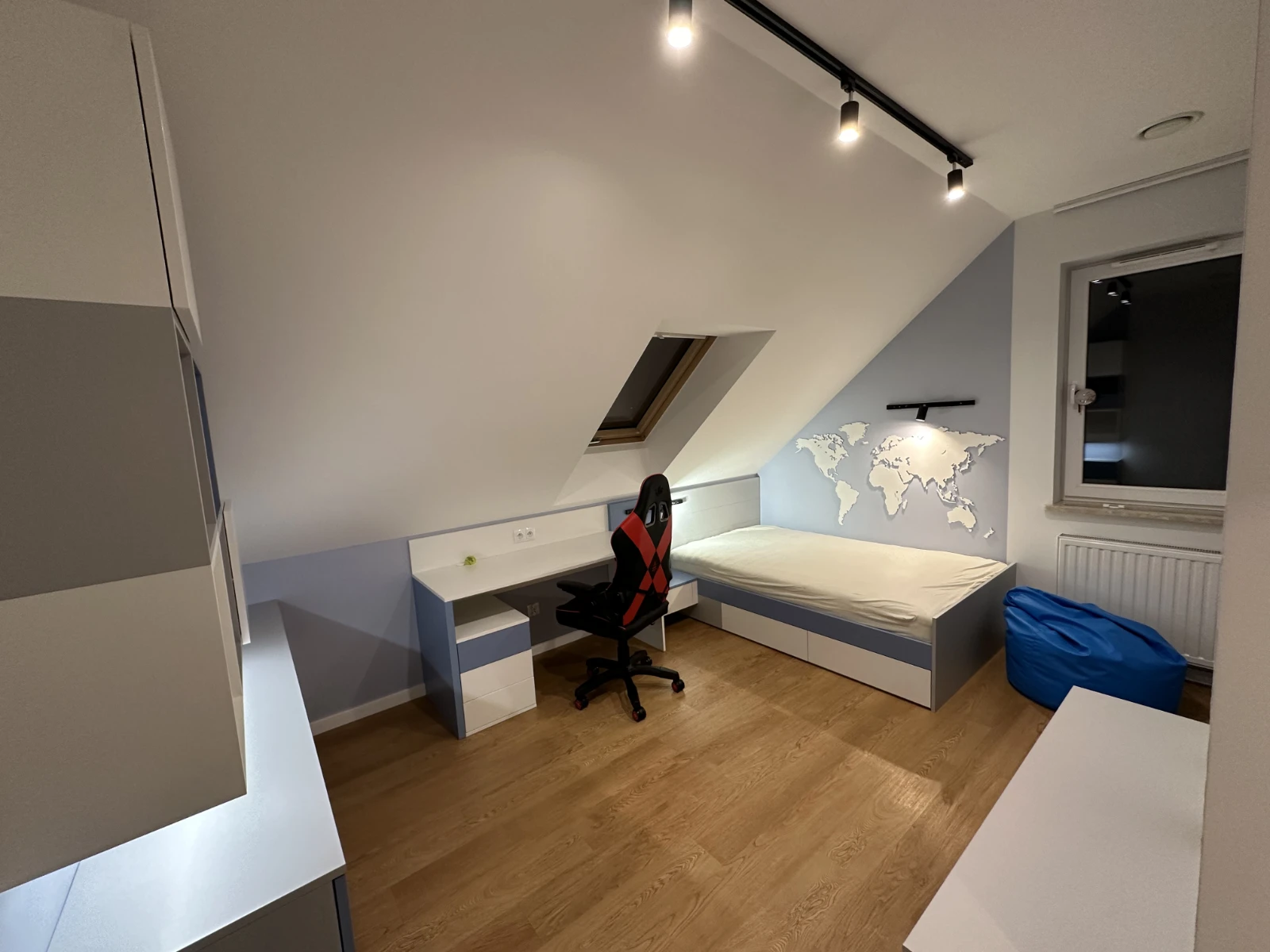 Mała sypialnia z mapą świata na ścianie, biurkiem do nauki i niebieskimi akcentami