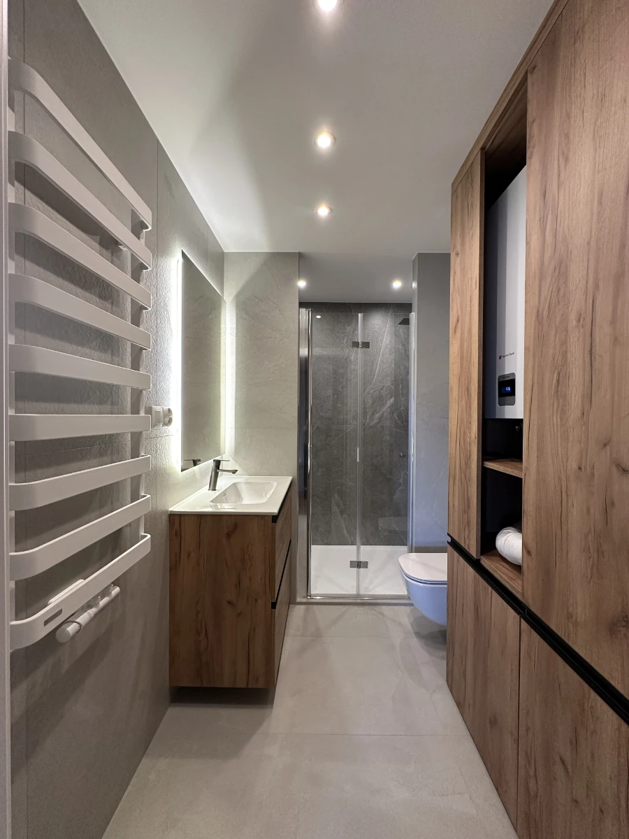 Widok na łazienkę od drzwi wejściowych z drewnianą szafą po prawej stronie