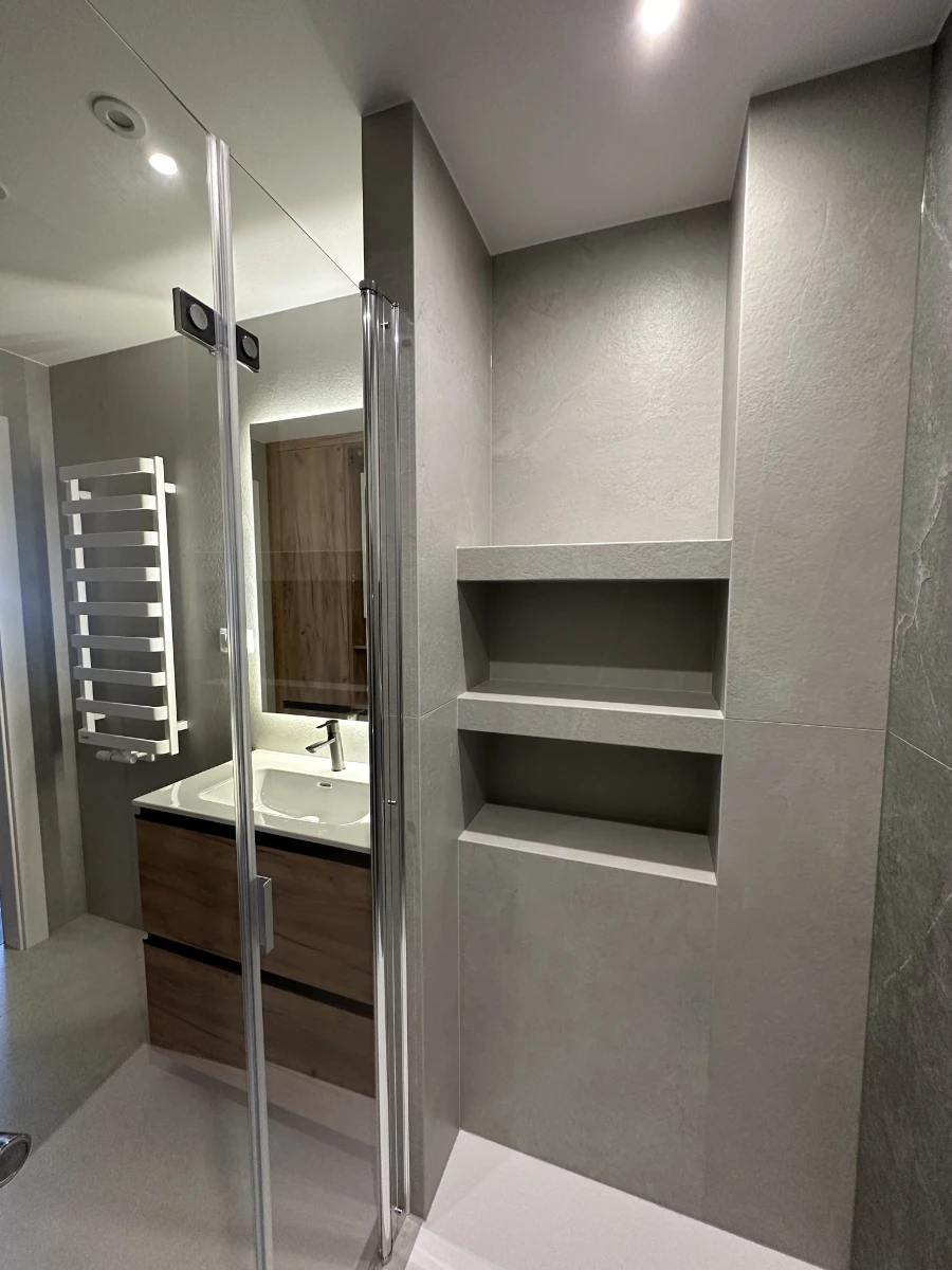 Widok ze środka kabiny prysznicowej z szarą ścianą i wnęką na półki