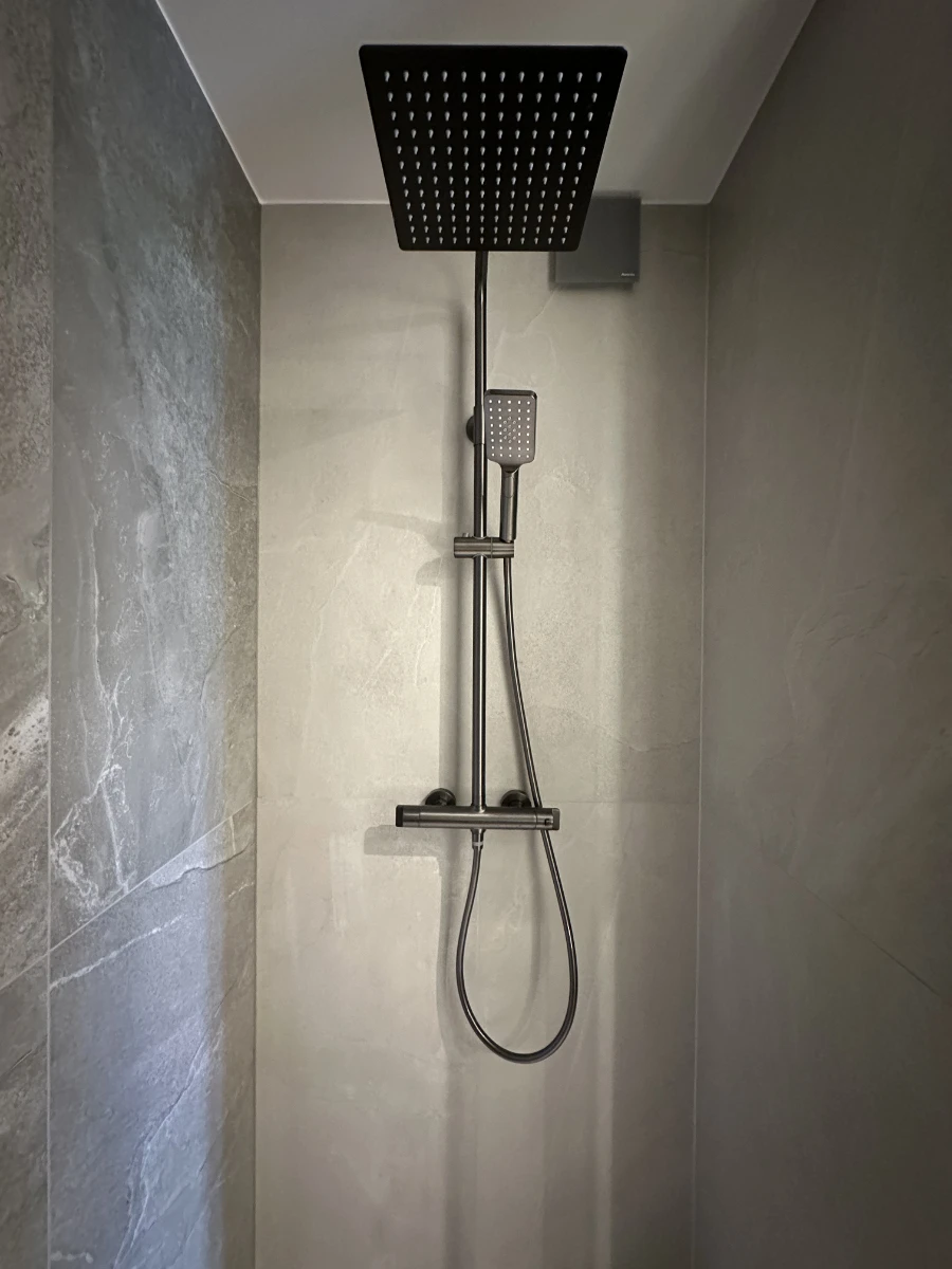 Kabina prysznicowa z nowoczesną armaturą, szarymi płytkami i dużą deszczownicą