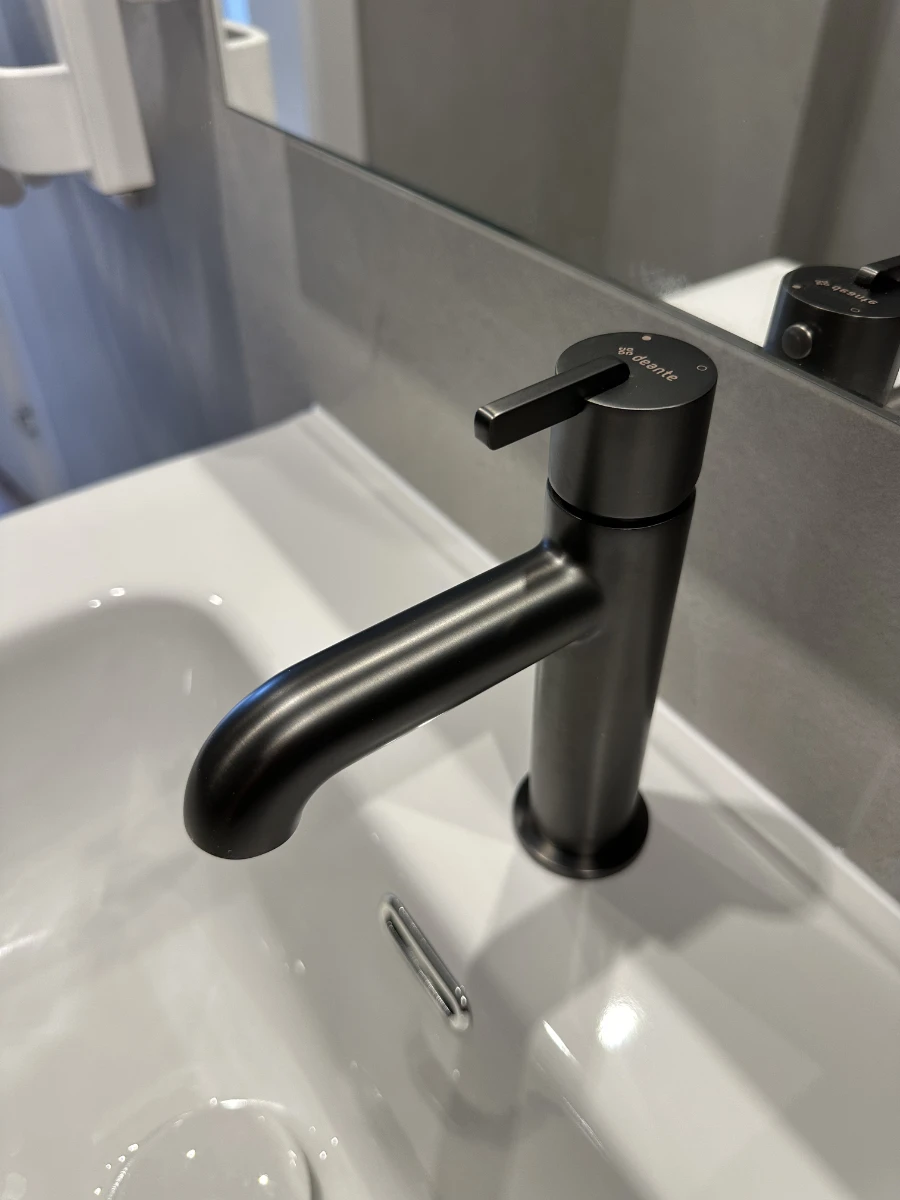 Szare płytki w łazience z widokiem na fragment zlewu i czarny minimalistyczny kran