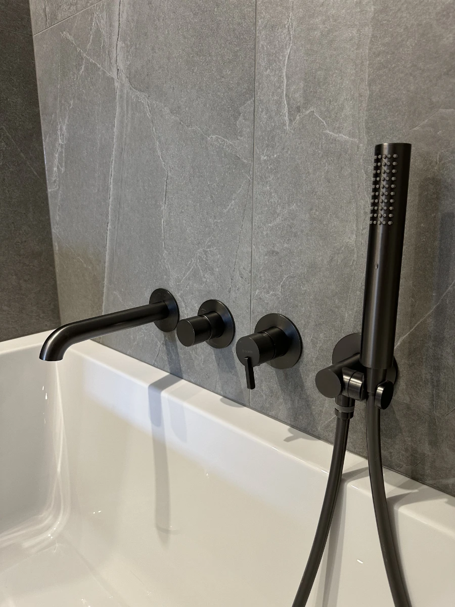 Szare płytki w łazience z wanną i nowoczesnym czarnym kranem oraz słuchawką prysznicową