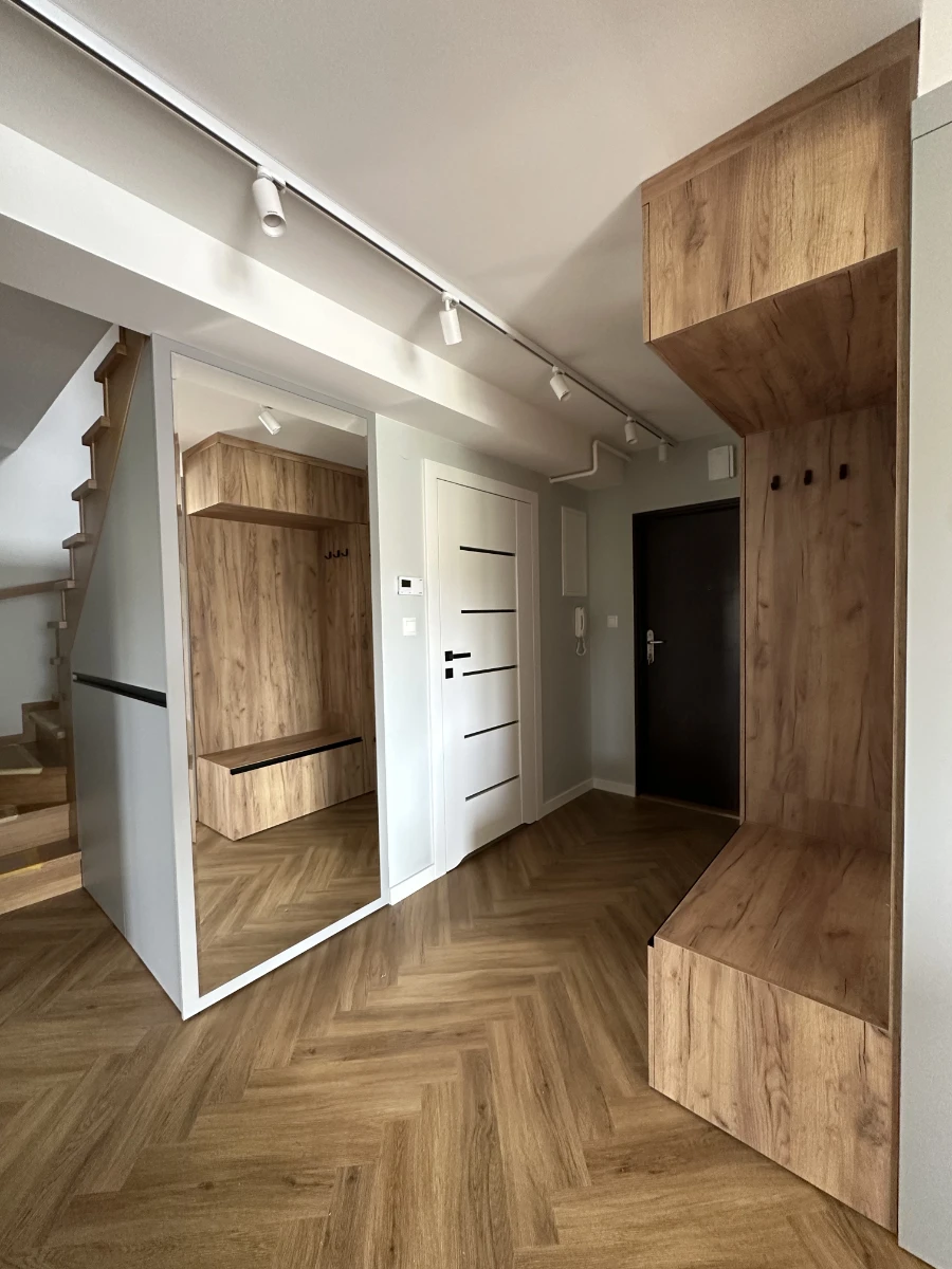 Przedpokój z mocnym drewnianym wykończeniem, lustrem po lewej i drewnianymi schodami prowadzącymi na piętro