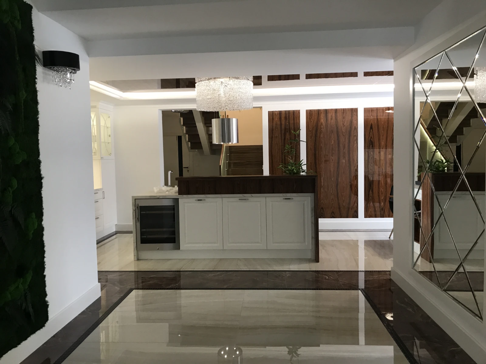 Widok na wyspę kuchenną od tyłu z dekoracyjnym lustrem i podświetleniem na ścianie po prawej