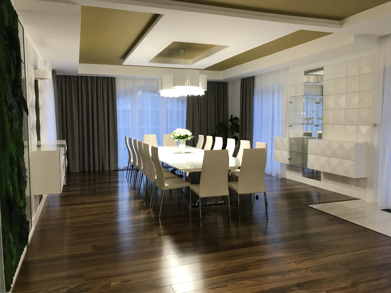 Jadalnia z długim białym stołem, wieloma białymi krzesłami, dużym lustrem i dekoracyjnymi płytkami na ścianie